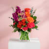 Bouquet of orange and magenta flowers in a clear glass vase with a happy birthday sign