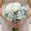 A small, hand-tied bouquet featuring white roses, light blue hydrangea, and baby's