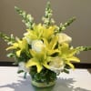 Yellow lilies and white roses arranged in a green glass vase