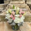 Pink roses and white lilies arranged in a glass vase with white hydrangeas