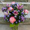 Pink roses, lilies, and purple daisies in a glass vase