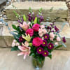 Bouquet of pink roses, lilies, and purple daisies in a glass vase