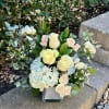 Arrangement of cream roses, pale hydrangea, and eucalyptus in a square glass vase