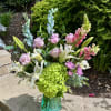 Mixed bouquet in a turquoise glass vase with lilies, roses, snapdragons, and hydrangea