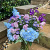 Bouquet of blue hydrangeas, pink roses, and purple flowers in a glass vase