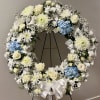 Large white floral wreath with blue hydrangeas on a black stand