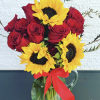 Red roses and yellow sunflowers in a clear glass pitcher with a red ribbon