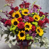 Bouquet of red roses, sunflowers, and purple flowers in a glass vase