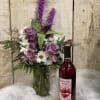 Purple and white bouquet in a glass vase beside a bottle of wine