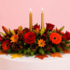 Autumn floral centerpiece with red roses, orange daisies, and two gold candles