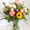 Mixed bouquet of roses, sunflower, and carnations in a glass vase