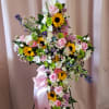 Large floral cross with pink roses, sunflowers, and white daisies on a stand