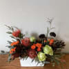 Orange and green floral arrangement in a white rectangular container