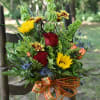 Mixed bouquet of red roses, yellow blooms, and blue thistle in a glass vase