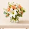 Peach roses and white lilies arranged in a clear glass vase