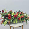 Long rectangular floral arrangement with red and pink blooms and pomegranates