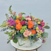 Mixed bouquet of orange, pink, and purple flowers in a white vase