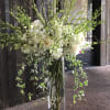 Tall white floral arrangement in a clear glass vase with trailing ivy