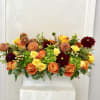Mixed bouquet of orange, yellow, and burgundy flowers in a white container