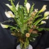 White calla lilies arranged in a clear glass vase with green accents