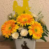 Orange gerbera daisies and white roses in a glass vase with a yellow cowboy topper