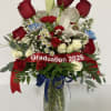 Red roses and white lilies in a glass vase with a graduation ribbon