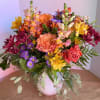 Mixed bouquet of pink, orange, yellow, and purple flowers in a white vase