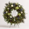 Large floral wreath with white roses, blue flowers, and peacock feathers on a stand
