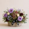 Mixed bouquet in a low stone container with purple, cream, and burgundy blooms