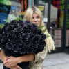 Woman holding a large bouquet of black roses with greenery