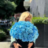 Woman holding a large bouquet of bright blue roses in a black vase