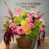 Pink and yellow floral arrangement in a wicker basket with green accents