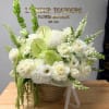 White floral arrangement in a wicker basket with green accents