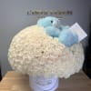 White rose arrangement in a round box with a blue teddy bear on top