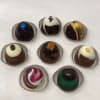 Assortment of eight decorated round chocolate truffles in paper cups on a white surface