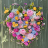 A lush, heart-shaped tribute overflowing with large peonies and ranunculus makes an