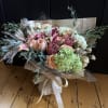 Bouquet of peach roses, hydrangeas, and dried grasses wrapped in newspaper