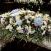 Large white floral casket spray with blue hydrangeas and purple accents