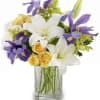 Mixed bouquet of white lilies, yellow roses, and purple irises in a clear glass vase