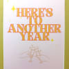 Greeting card with “Here’s to Another Year” text and hands clinking champagne glasses.
