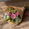 Hand-tied bouquet of pink, white, and purple flowers in brown paper