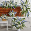 Blue and white floral funeral arrangements around a wooden casket