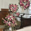 Pink floral wreaths and a large bouquet arrangement on stands in a church interior.