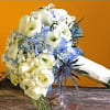 Hand-tied white and blue bridal bouquet with roses, calla lilies, hydrangea and thistle on a rustic surface