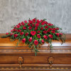 Red rose casket spray with trailing greenery on a wooden casket