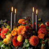 Orange and red flowers arranged with four lit black candles