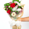 Handheld mixed bouquet with red roses, white mums, and pastel blooms wrapped in cellophane with a white bow
