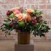 Mixed bouquet of peach roses, pink daisies, and green mums in a gold vase
