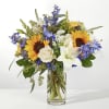 Bouquet of sunflowers, white lilies, and blue flowers in a clear glass vase