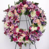 Large floral wreath with pink lilies, roses, and purple daisies on a stand